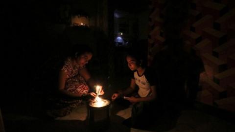 A woman and her daughter light a candle inside their house after a power outage in Mumbai, India, October 12, 2020.