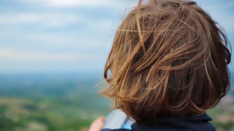 Child with long hair, seen from behind, looking at a landscape