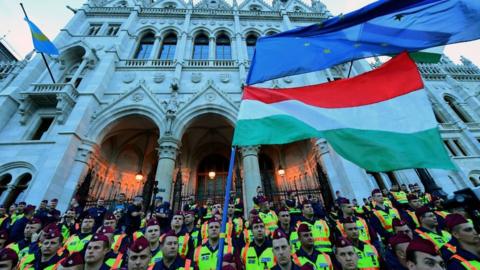 People protest in front of lines of police officers at the parliament building at Budapest