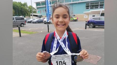 A girl smiling holding medals won at the British Transplant Games