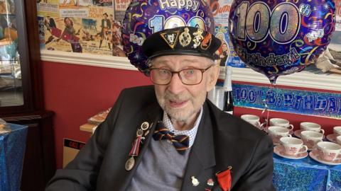 Dennis Lanham stood in front of some "Happy 100th Birthday" balloons and a table full of teacups ready for a party