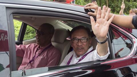 Anwar Ibrahim waves at his supporters as he arrives at a polling station