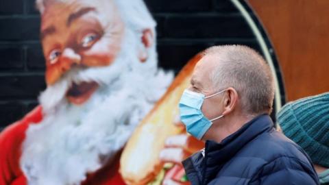 A man wears a mask near a picture of Father Christmas