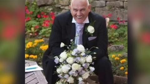 Richard Reeves smiling holding a bunch of white flowers