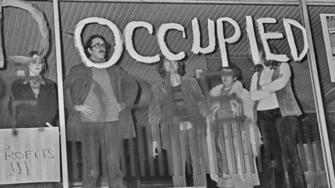 Black and white photo of protesters occupying the Centre Point building with "occupied" daubed over the window