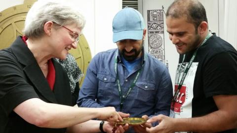 Volunteers Tammam and Abdullah examine an astrolabe with museum director Silke Ackermann