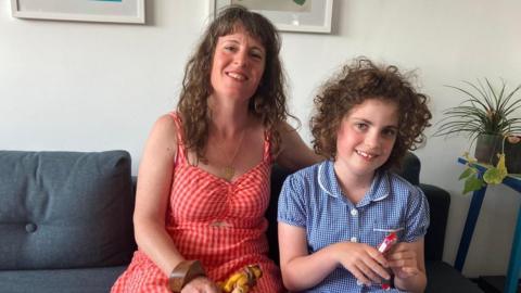 A mum in a red dress and a young child in her school uniform