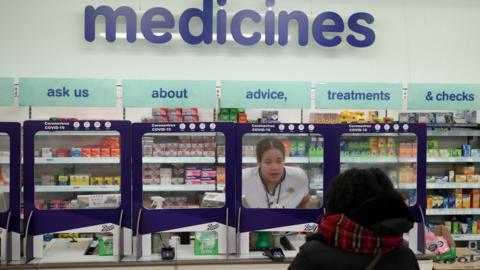 A Boots pharmacist speaking to a customer from behind a safety screen