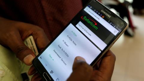 An employee assists a customer to set-up M-Pesa money transfer servive on his handset inside a mobile phone care centre operated by Kenyan"s telecom operator Safaricom; in the central business district of Kenya"s capital Nairobi, May 11, 2016.