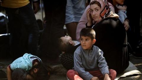 Syrian refugees and migrants wait with children at a registration camp in Presevo after their arrival in Serbia on 30 August 2015