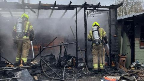 Firefighters in the charred remains of an outbuilding