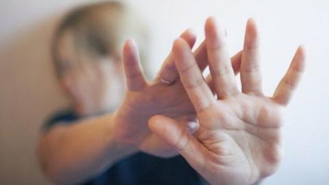 A woman holds out her hands to protect herself