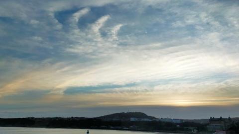 Milky skies with wispy clouds over a harbour.