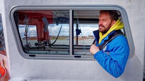 Christian Zemann on his ferry with arm through window wearing a blue jacket