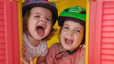 Two girls wearing cycle helmets looking through the window of a playhouse