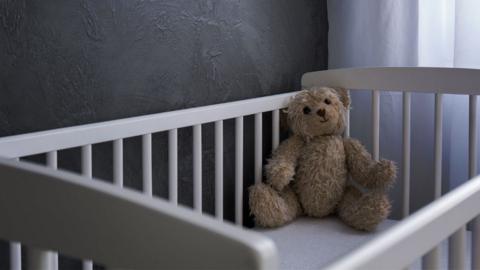 An empty cot with a teddy bear toy (generic)