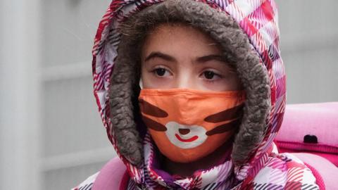 A child wearing a face mask arrives at school in New York City