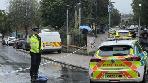 A police officer in a yellow jacket standing in front of a police tape