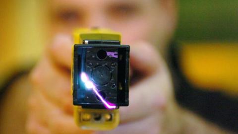 Out of focus person holding a taser to the camera