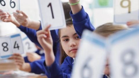 Pupils in class holding up number cards - stock photo