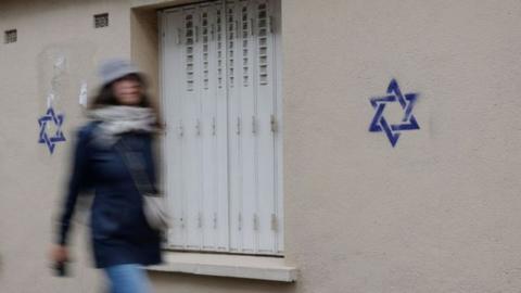 A woman walks along a building whose facade is covered with Stars of David in Paris