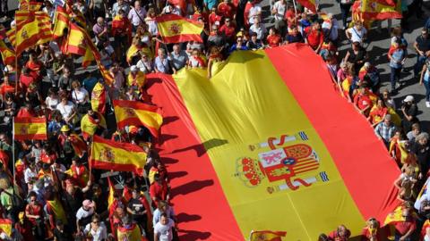 Image shows protesters holding a giant Spanish flag during a demonstration to support the unity of Spain on 8 October 2017