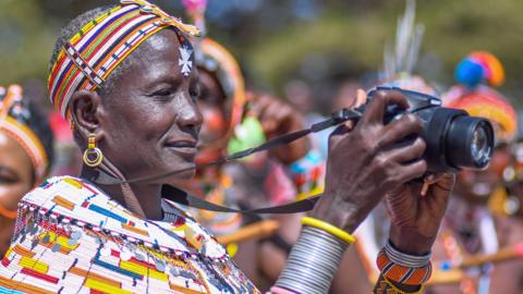 A Kenyan woman in traditional dress holding a camera head of the Maralal International Camel Derby in Yare, Samburu, Kenya - Saturday 7 October 2023