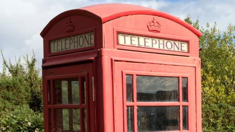 Stock image of a red phone box with trees behind it