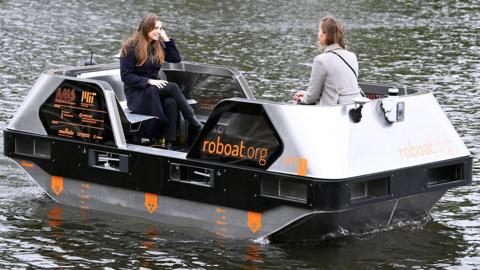 Two people sit on a robot boat sailing on a canal in Amsterdam
