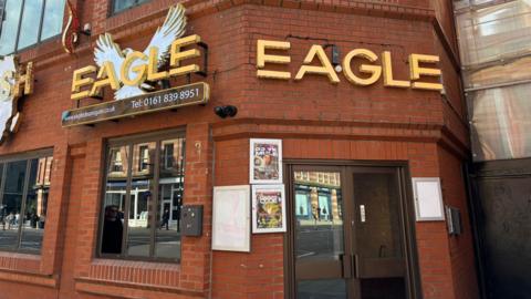 A red brick building with brown framed windows and door. Eagle is written on the front in gold letters 