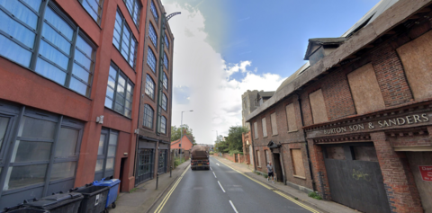 College street, on the right an old factory building with boarded up windows, on the left is a block of flats with red brick and black window frames. 