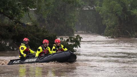 rescue workers in an inflatable dinghy traverse brown flood waters