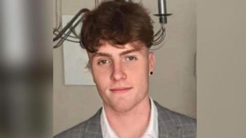 Tom Linton in a white shirt and grey suit jacket. He has brown hair and brown eyes.