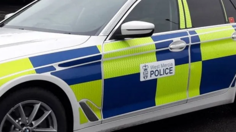 A close-up of a police car with blue and yellow hi-viz markings and a West Mercia Police logo