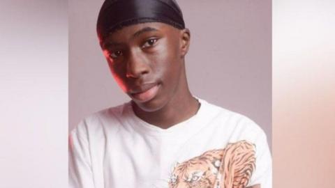 Jibrael Fehintola wearing a black cap on his head. He is looking at the camera and not really smiling. He is also wearing a white top with a tiger on the right hand side. 