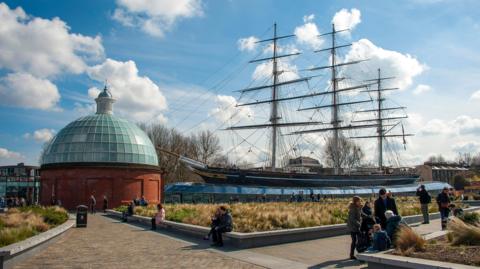 The Cutty Sark in dry dock. People are sitting nearby on a cold but sunny day.