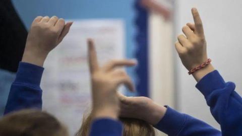 A group of children with their hands in the air. Their sleeves are all blue.
