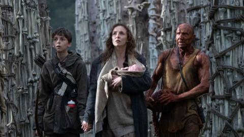 Spike, Jodie Comer holding a newborn, and Ralph Fiennes as Dr Kelson 