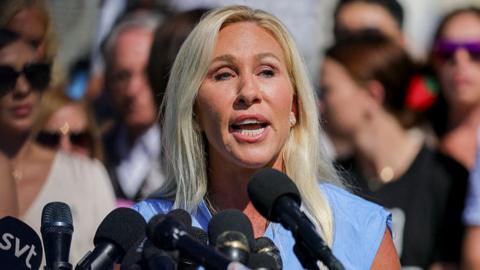 Green pictures giving a speach. She is wearing a blue outfit.