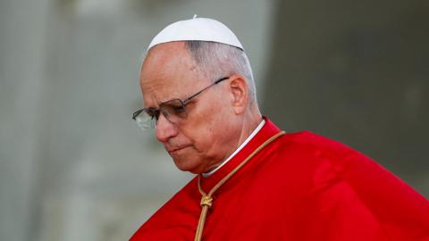 Pope Leo looks thoughtfully down to the left of the picture during his visit to Algeria on Monday. He is wearing glasses, a papal skull cap and red robe.