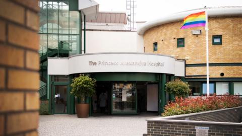The entrance to the Princess Alexandra Hospital with a rainbow flag flying on a vertical pole outside.