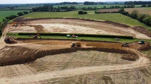 Diggers and tractors work on giant excavation of flood basins leaving tracks on soil over a vast area - see from the air