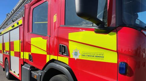 A close up stock photo of a red and yellow fire truck on the passenger side door are the words 'Cambridgeshire Fire and Rescue Service'. 