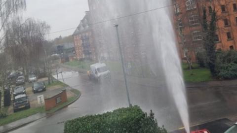 Water shooting into the air in a residential area, climbing higher than the lamppost