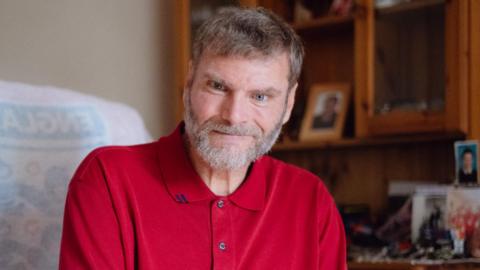 Paul Chandler in a red shirt with a serious face