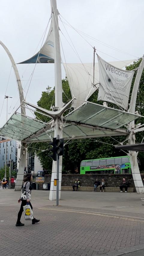 A white sail structure placed near a road with shops in the background.