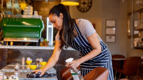 Woman in an apron cleans table in a cafe.