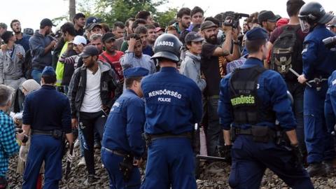 Refugees are stopped by police officers as they walk on the railway tracks near Szeged town in September 2015