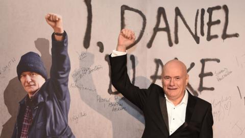 Dave Johns in front of a poster for I, Daniel Blake at the film's premiere in 2016