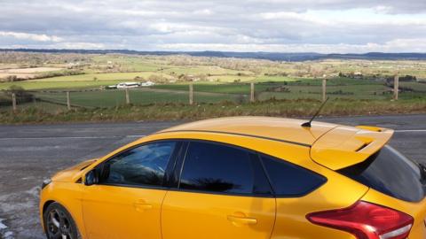 Yellow car parked in layby overlooking countryside